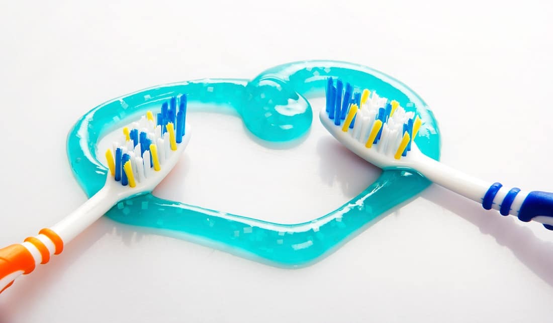 Two toothbrushes with colorful bristles beside a turquoise fish-shaped dental guide holder.