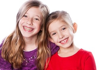 Two young girls smiling brightly, showcasing healthy teeth and happy expressions.