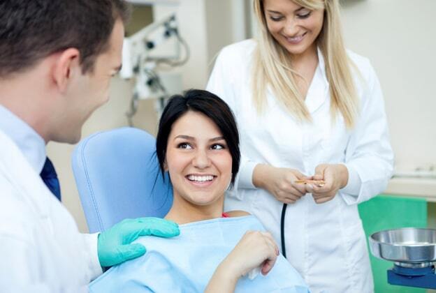 Smiling patient in dental chair with dentist and hygienist discussing gum disease treatment.