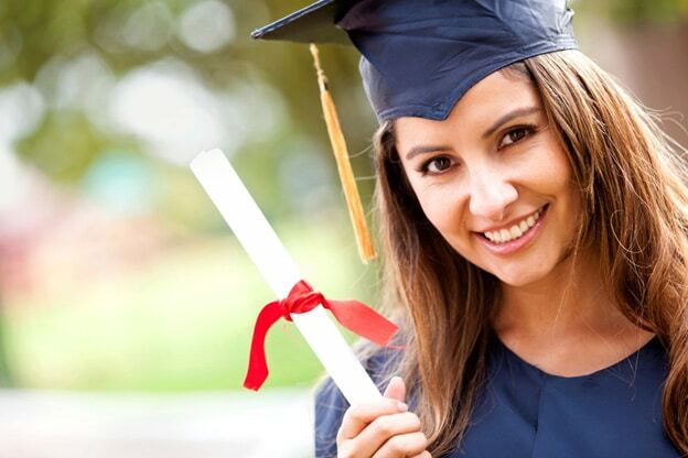 Young woman in graduation cap and gown holding diploma with red ribbon, smiling.
