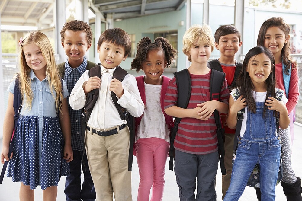 Group of diverse elementary school children smiling in school hallway.