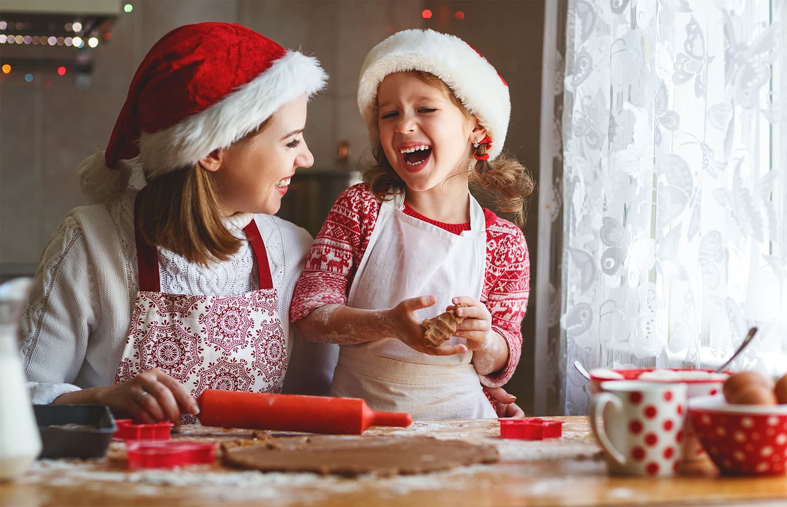 Happy mother and daughter baking holiday cookies together in festive Santa hats.