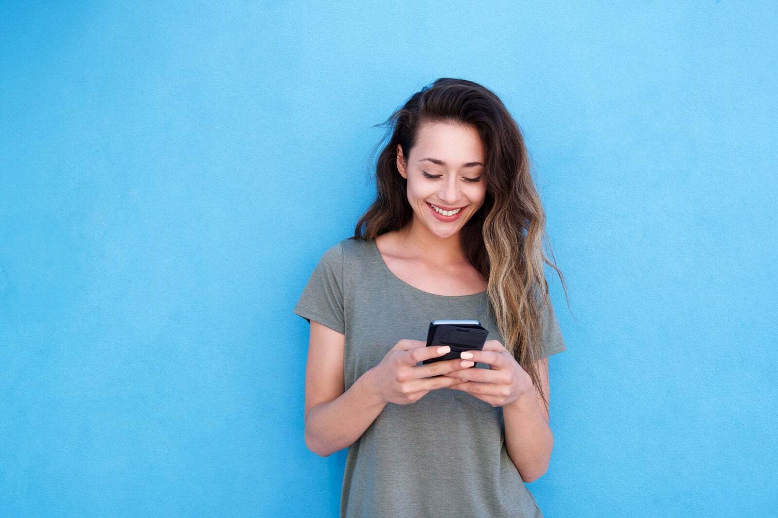 Smiling woman in gray shirt holding mobile device against blue background.