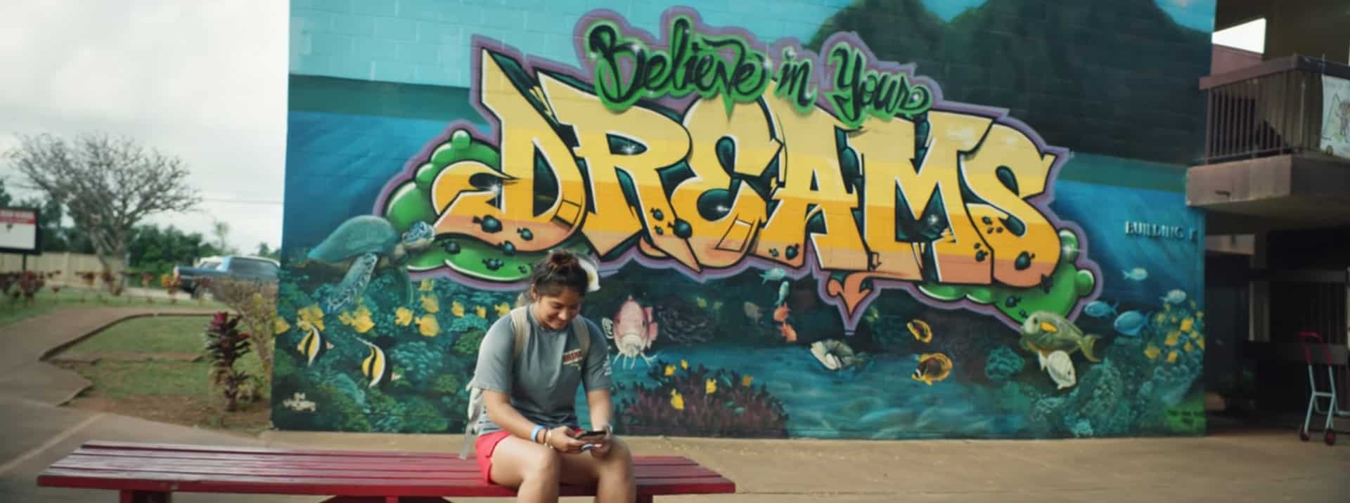 Student athlete posing in front of colorful "Believe in Your Dreams" mural in Corpus Christi.