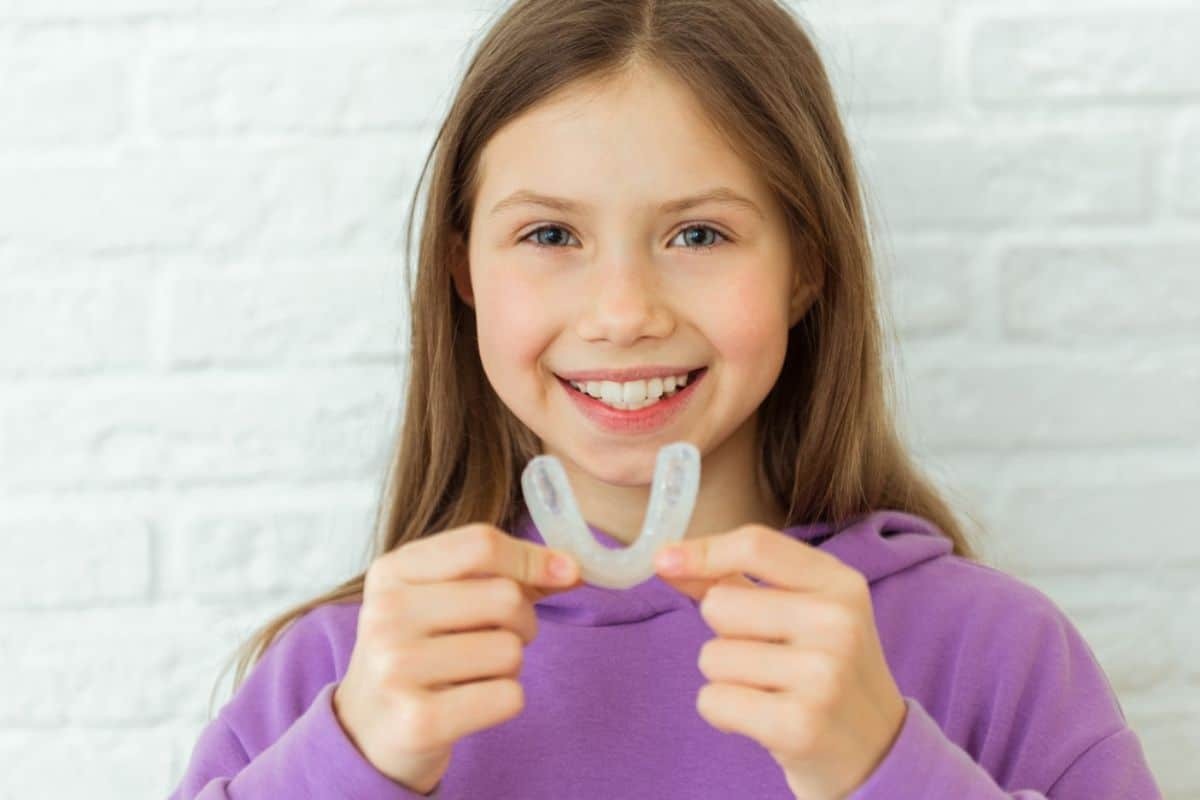 Young girl holding clear sports mouthguard and smiling at camera.