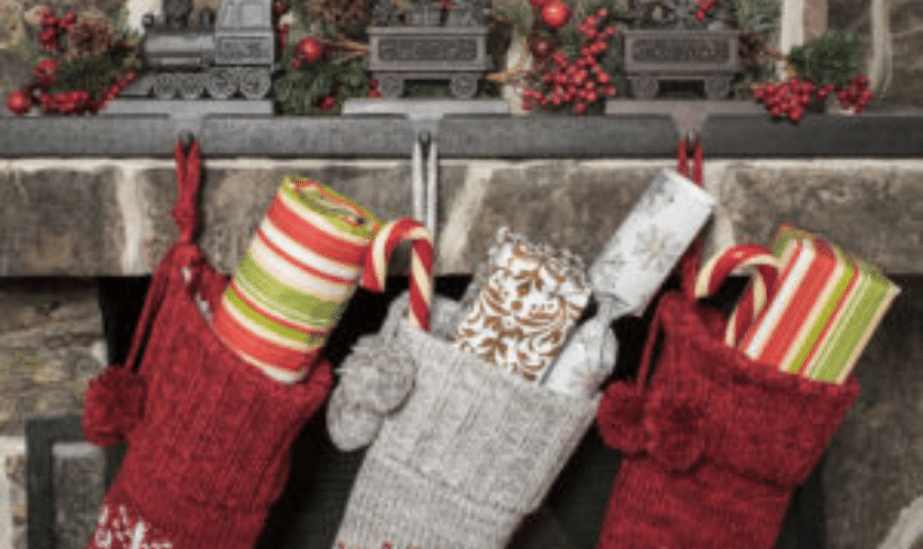 Red and striped Christmas stockings hung on a mantle with festive decorations.