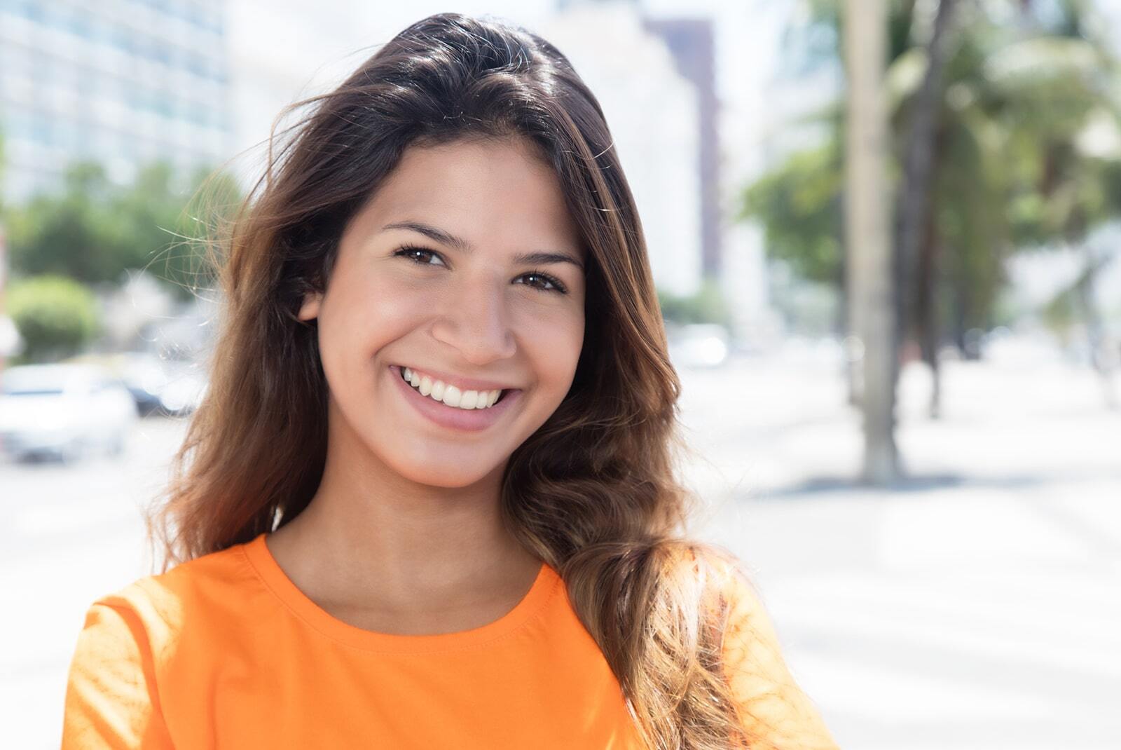 Woman smiling in orange shirt showcasing healthy teeth and bright smile in Corpus Christi.