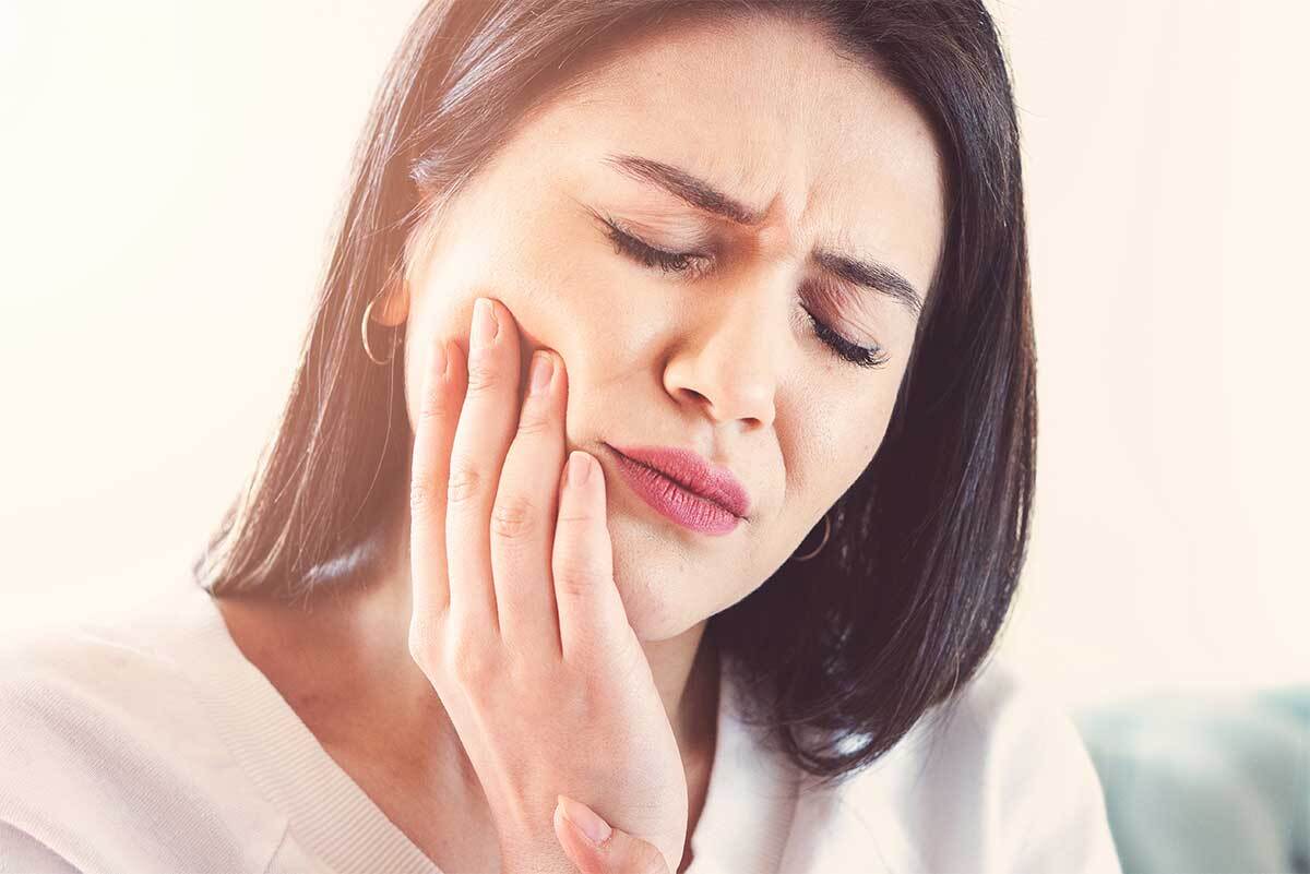 Woman holding her cheek with a pained expression, experiencing gum sensitivity.