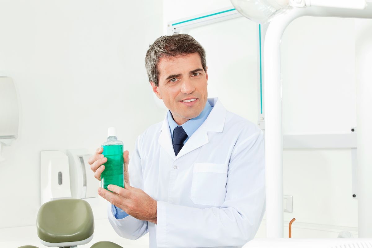 Dentist holding green mouthwash bottle in modern dental office treatment room.
