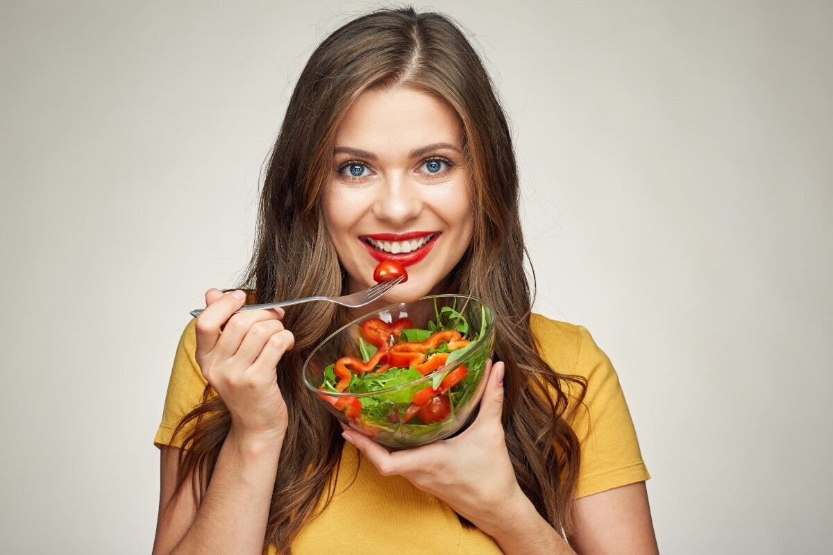 Woman eating healthy salad with red peppers and greens for optimal dental health.