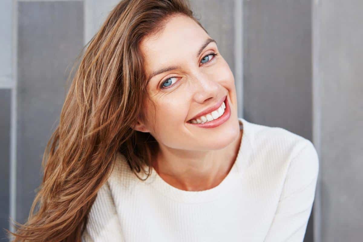 Woman smiling with healthy white teeth in dental office setting.