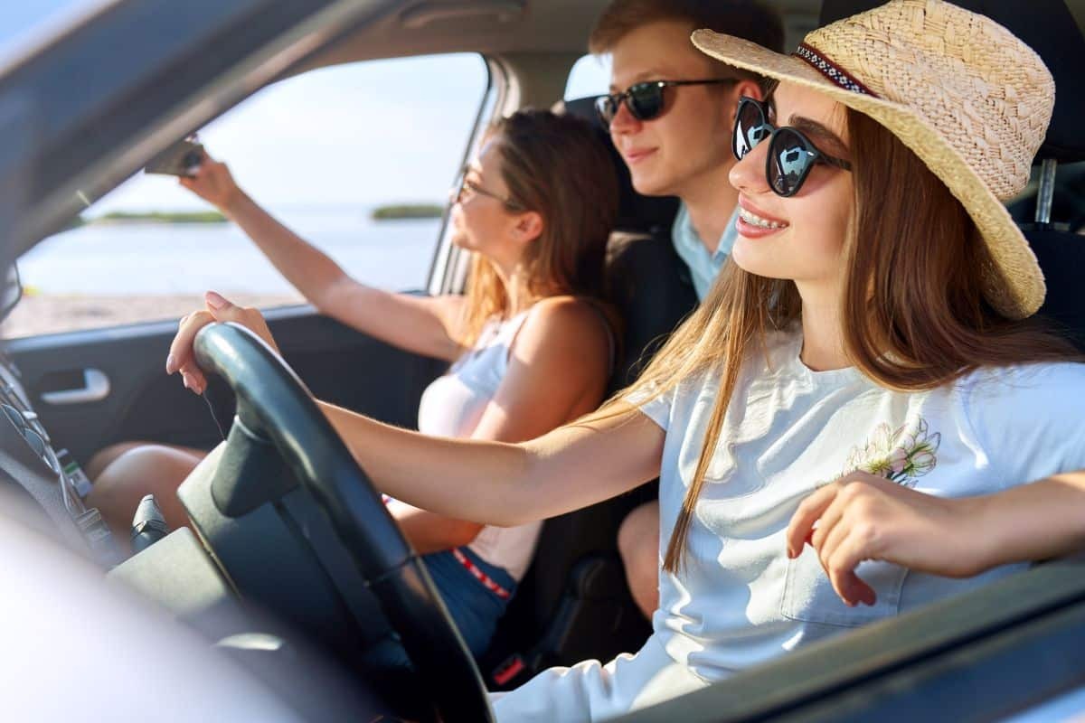 Young woman driving a convertible with friends, smiling while traveling with braces.