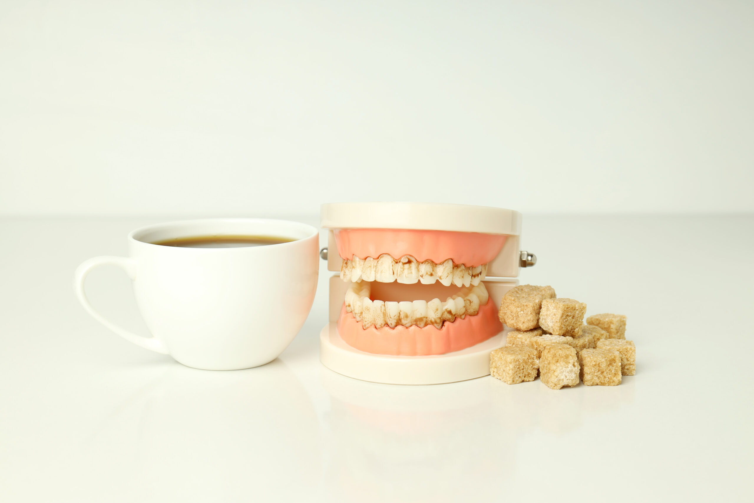 Dental model with dentures, coffee cup, and sugar cubes illustrating food impact on denture care.