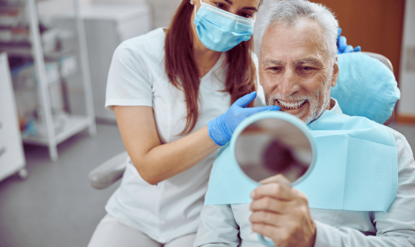 Senior patient admiring his new smile in mirror with dentist at Corpus Christi dental practice.