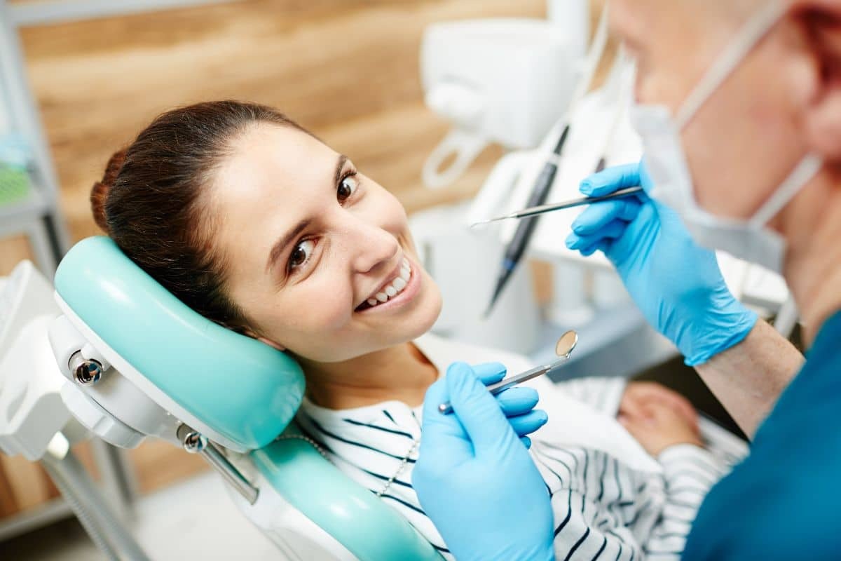 Smiling patient in dental chair receiving examination from dentist in blue gloves.