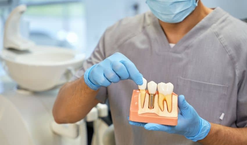 Dentist demonstrating dental implant model with crown and implant components in Corpus Christi office.