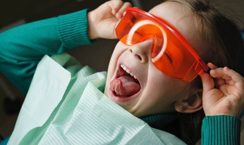 Happy child wearing red glasses holding dental care materials.