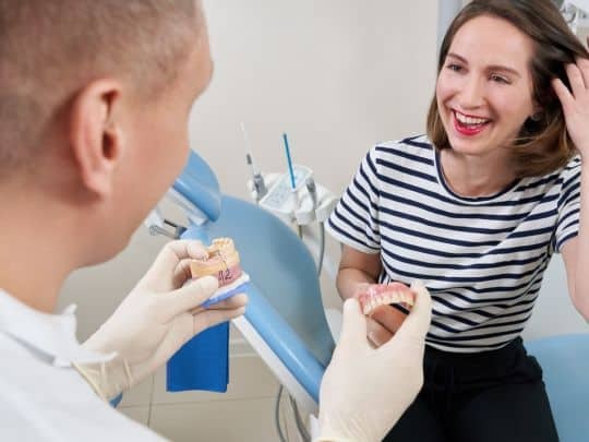 Dentist showing dental implant model to smiling patient in Corpus Christi office.