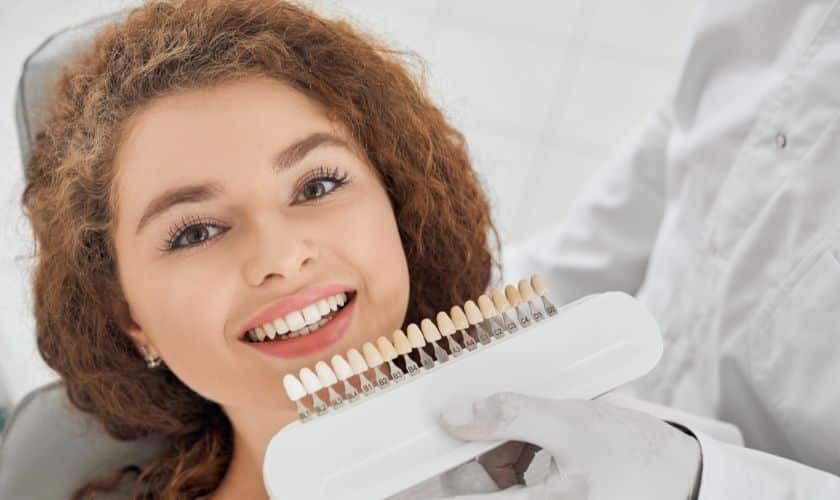 Woman smiling while holding dental shade guide showing tooth color options for implants.