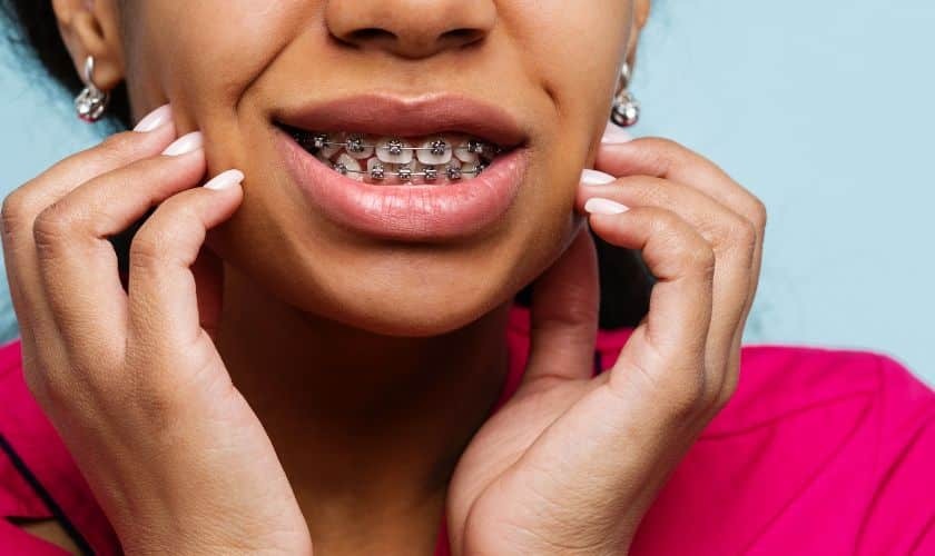 Young woman displaying metal braces with a confident smile against a blue background.