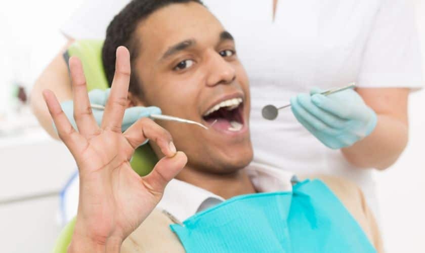 Man showing stop gesture during dental examination with dentist holding mirror.