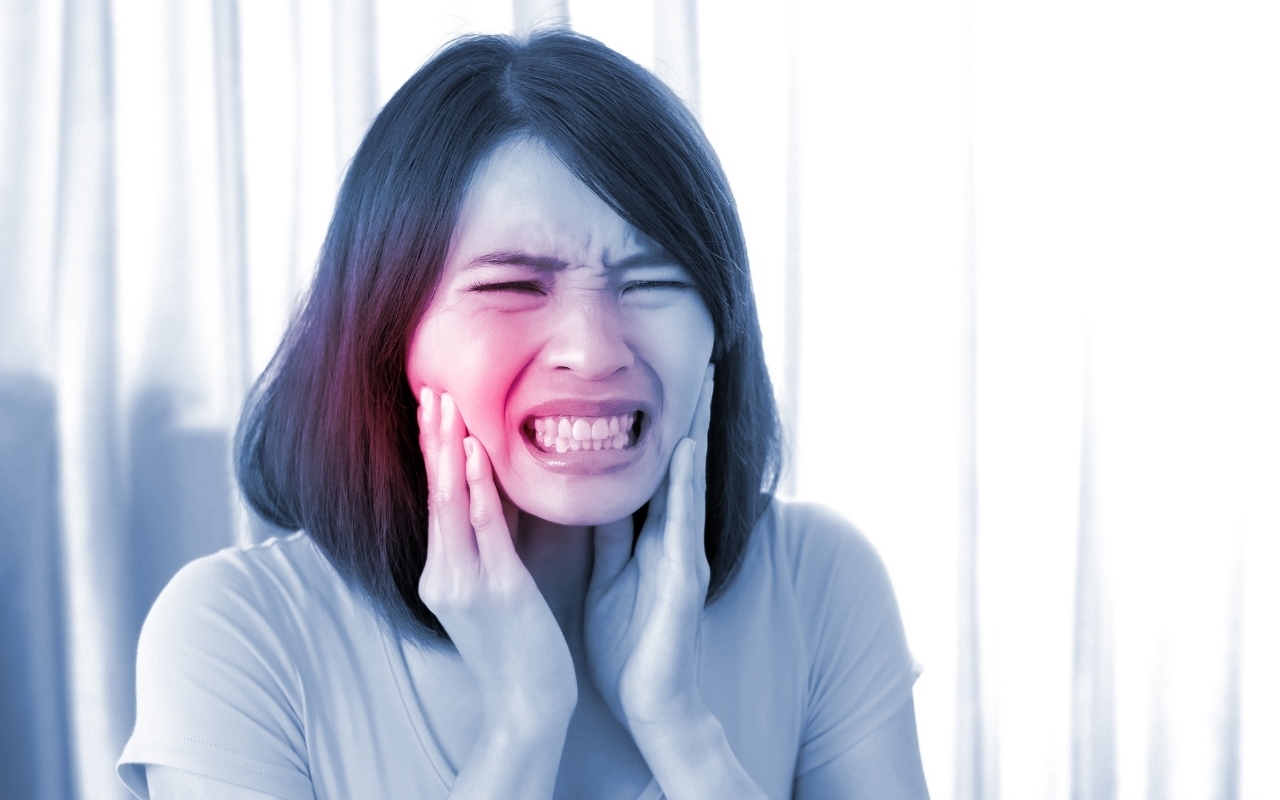 Woman experiencing tooth sensitivity pain, holding her cheek in discomfort.