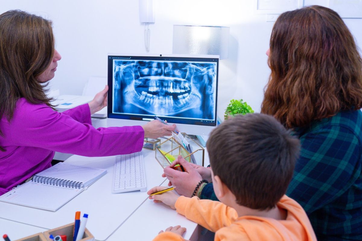 Dentist reviewing panoramic X-ray with parents and child during family dental consultation.