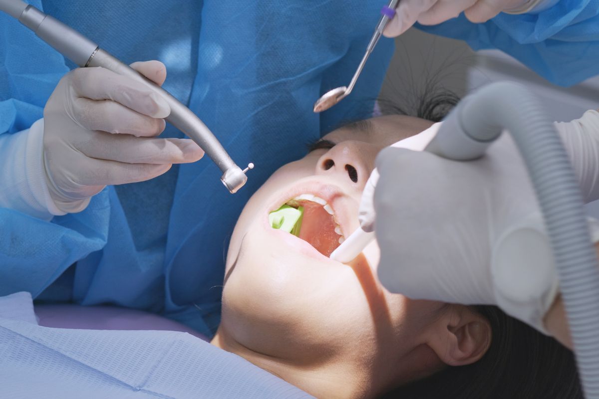 Pediatric dentist examines child's teeth during first dental visit using professional tools.