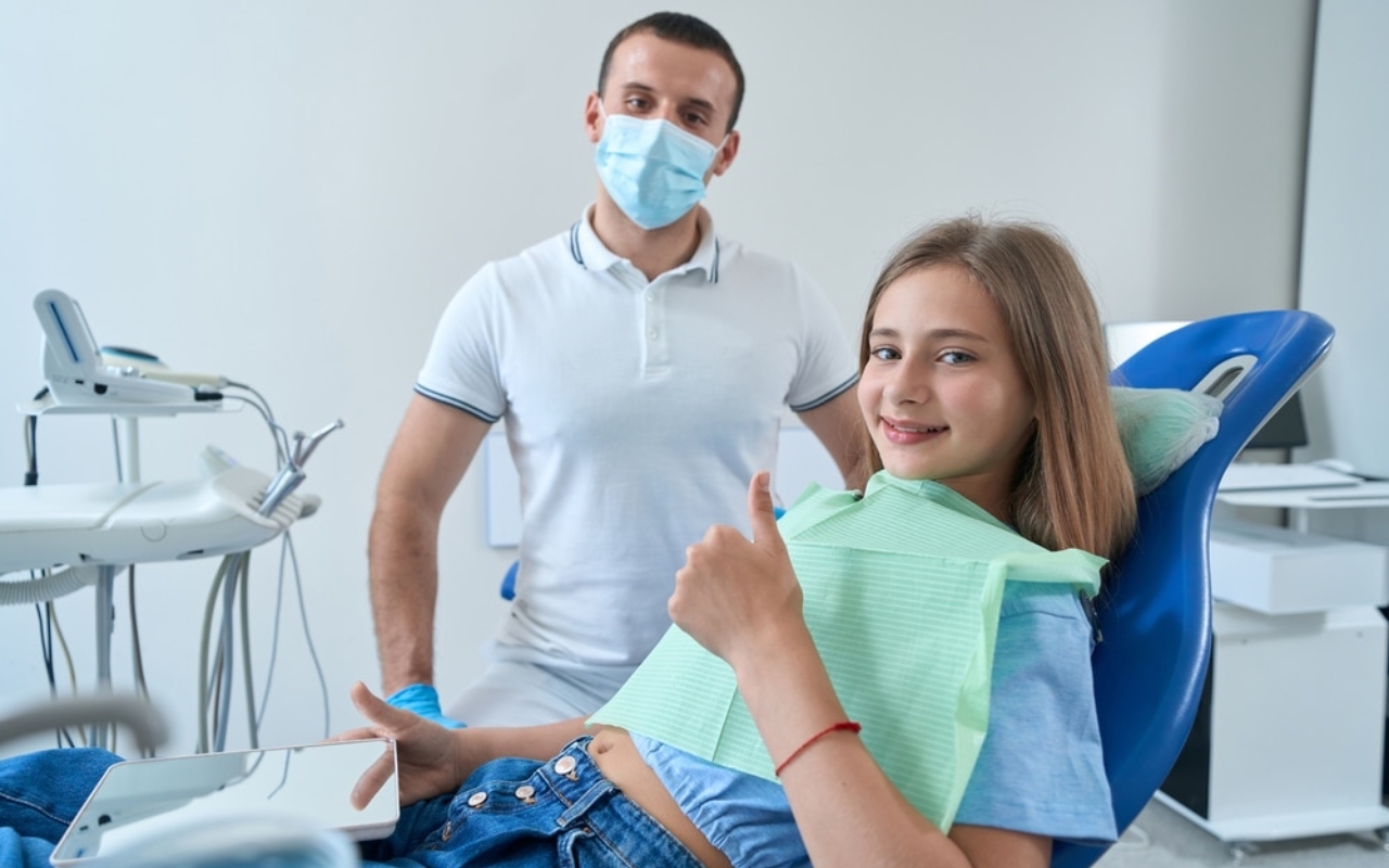 Young patient giving thumbs up in dental chair with dentist in mask at Corpus Christi practice.