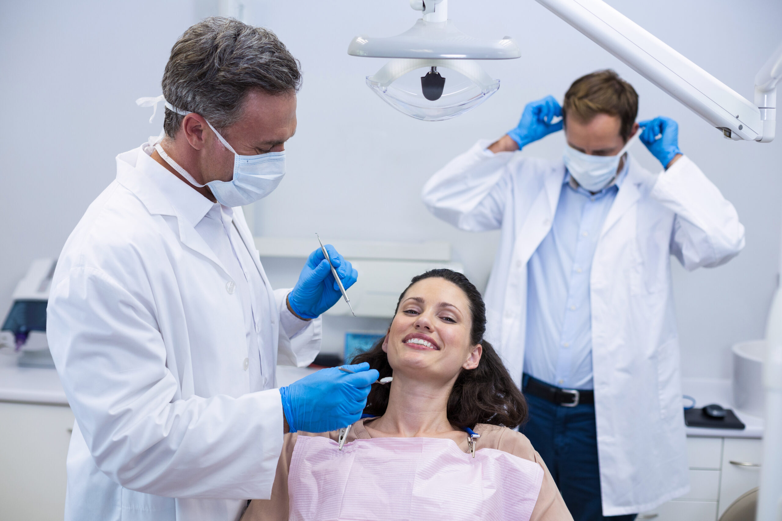 Dentist examining smiling patient's teeth in modern dental office with team assisting.