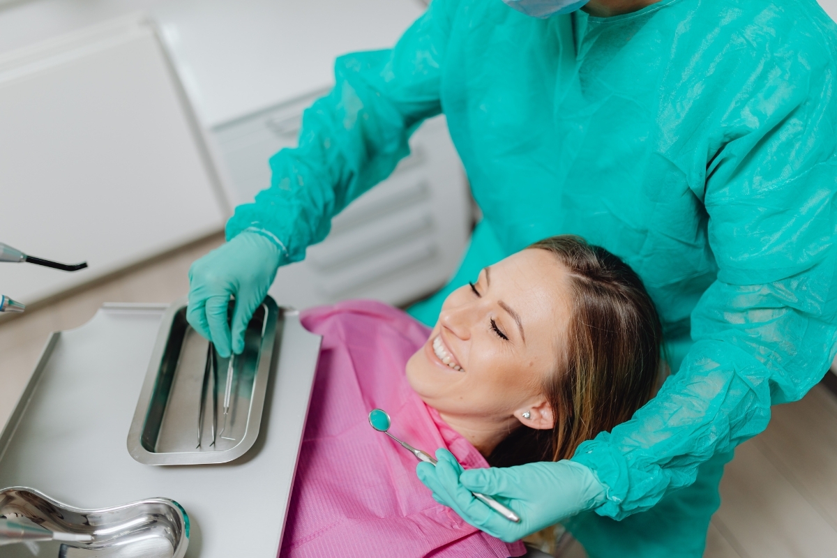 Smiling patient receiving dental care from dentist in turquoise scrubs during consultation.