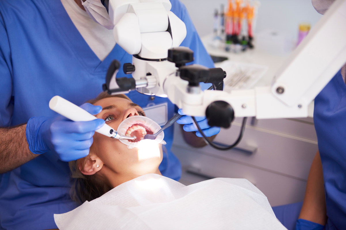 Dentist examining patient's teeth with mouth retractor during dental procedure in treatment room.