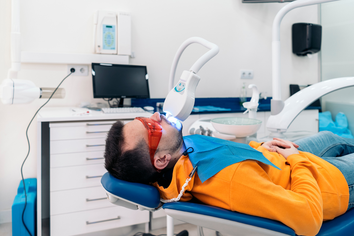 Young patient receiving LED teeth whitening treatment in modern dental office.