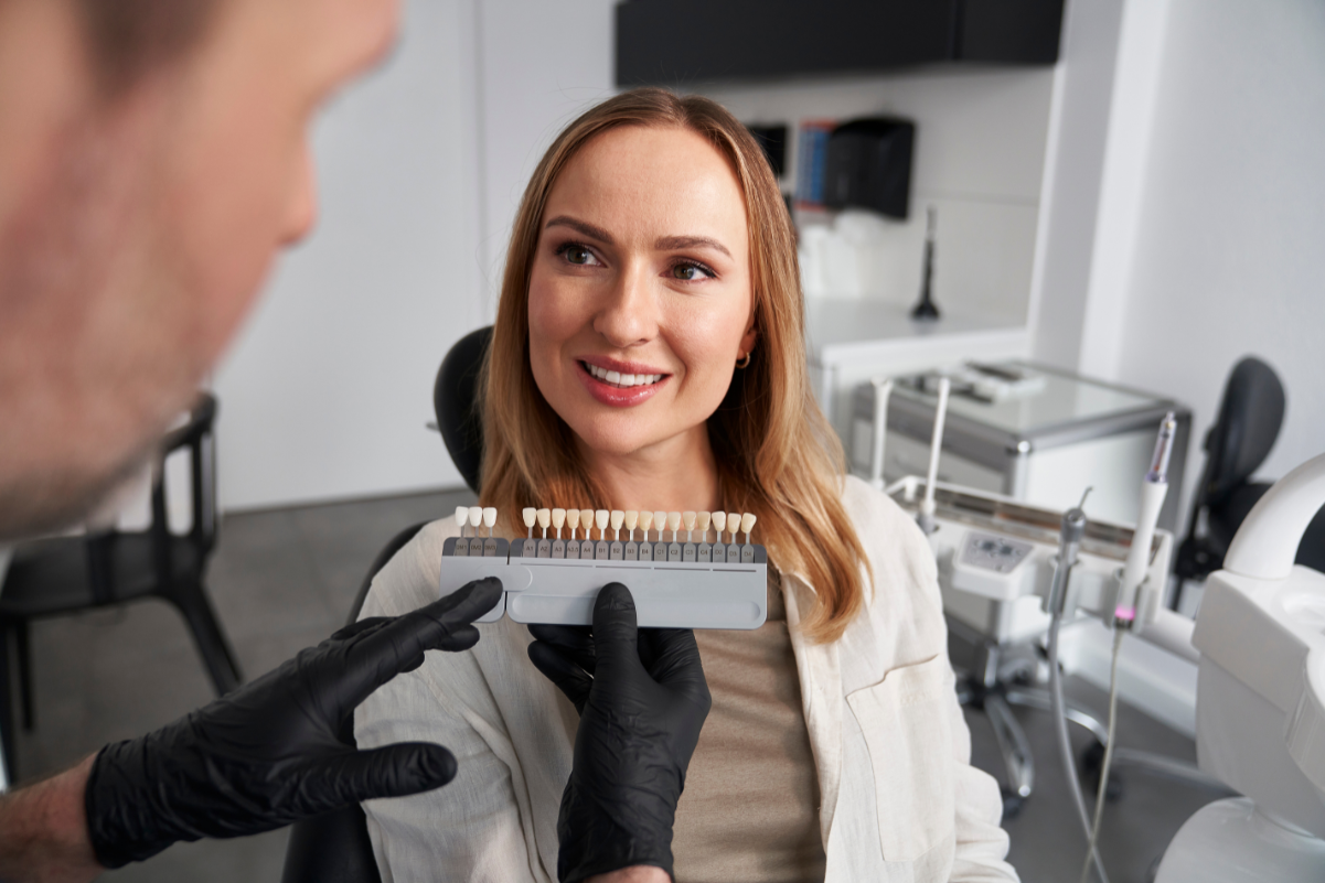 Dentist showing dental shade guide to smiling patient during smile makeover consultation.