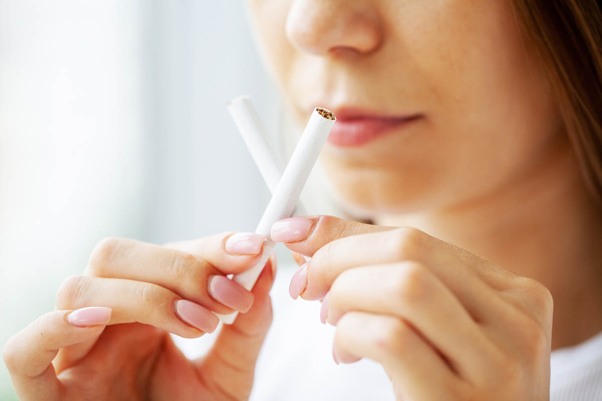 Woman breaking a cigarette in half, demonstrating smoking cessation for dental implant safety.